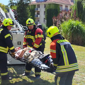 Übungsszenario an einer Klinik: Feuerwehrleute heben eine verletzte Person in Trage von der Drehleiter