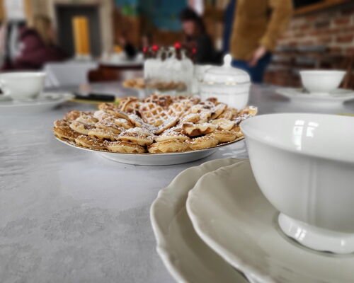 frische Waffeln unf Kaffeegedeck auf einem Tisch, im Hintergrund Personen