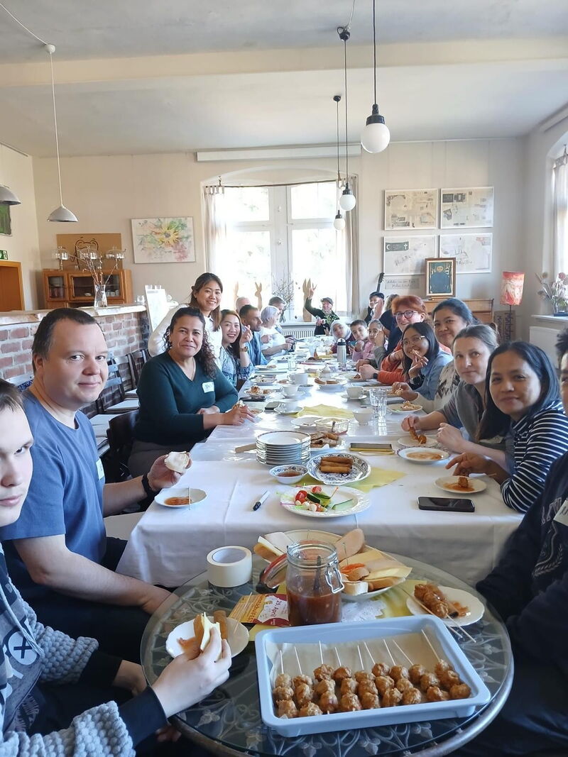 Zahlreiche Menschen unterschiedlicher Nationalität sitzen an einer langen Tafel und essen