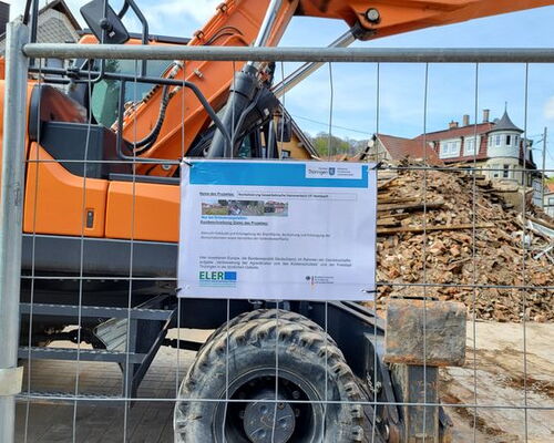 Detailaufnahme von Fördertafel mit Räumbagger hinter Bauzaun und einem großen Schutthaufen am Hammerteich in Steinbach