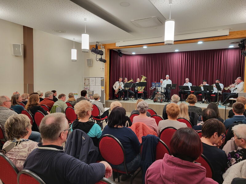 Saal mit Stuhlreihen und Menschen, auf der Bühne die Steinbacher Trachtenkapelle