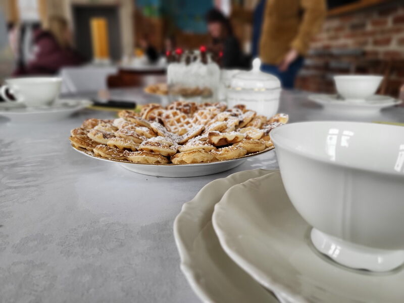 frische Waffeln unf Kaffeegedeck auf einem Tisch, im Hintergrund Personen