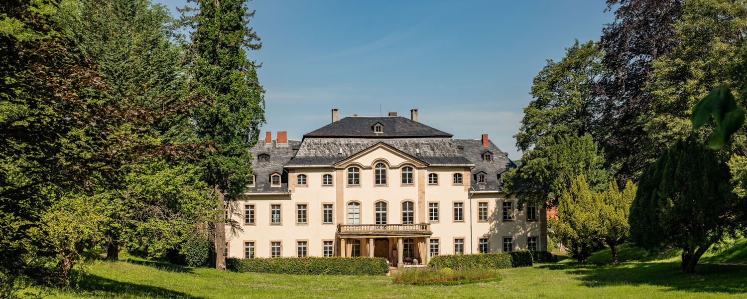 Parklandschaft mit Wiese, Bäumen und einem kleinen Schloss