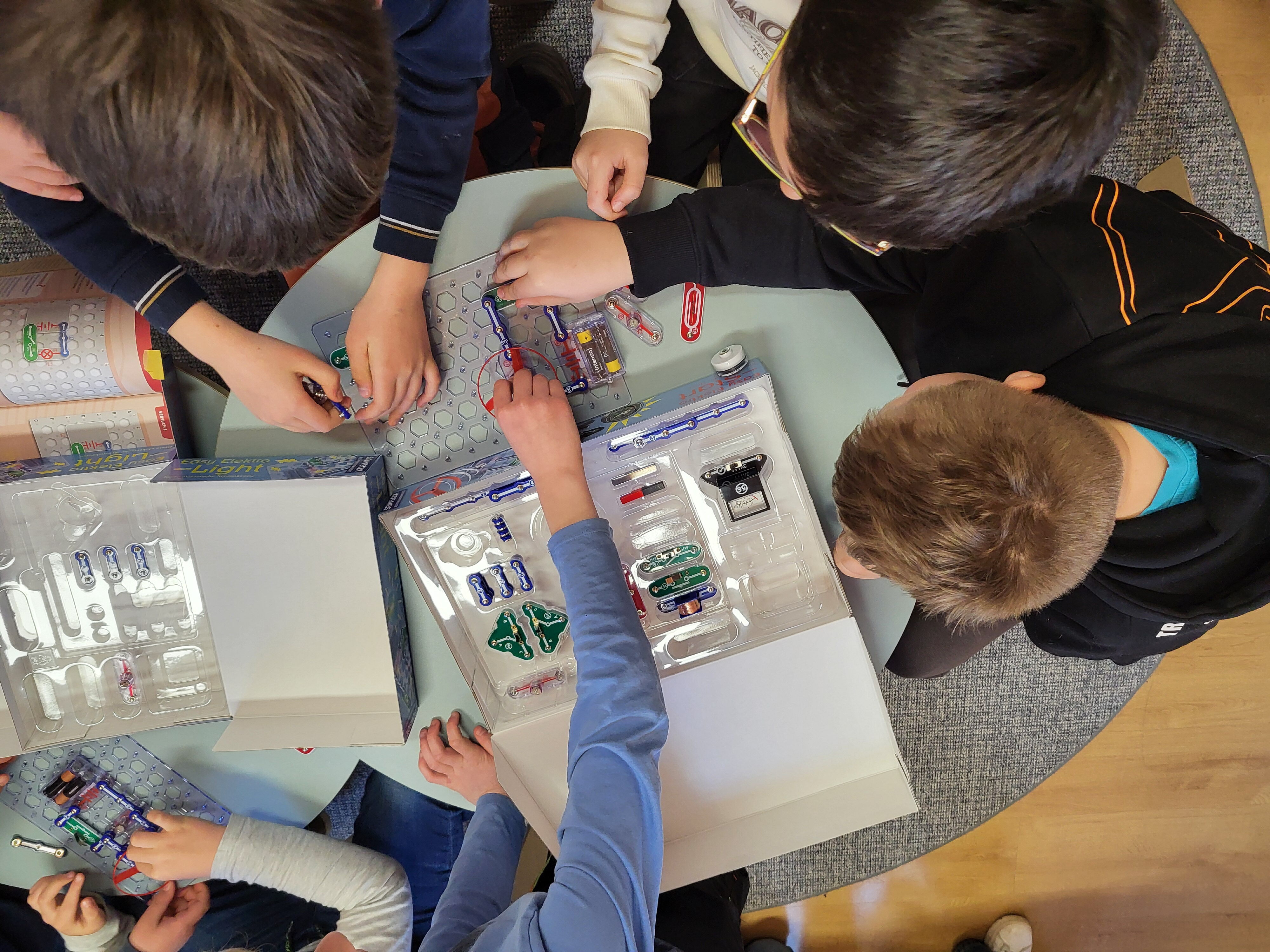 Konstruktionsplatte eines Elekrobaukastens von oben, viele Kinderhände sind gerade am Bauen, man sieht hauptsächlich ihre Hände